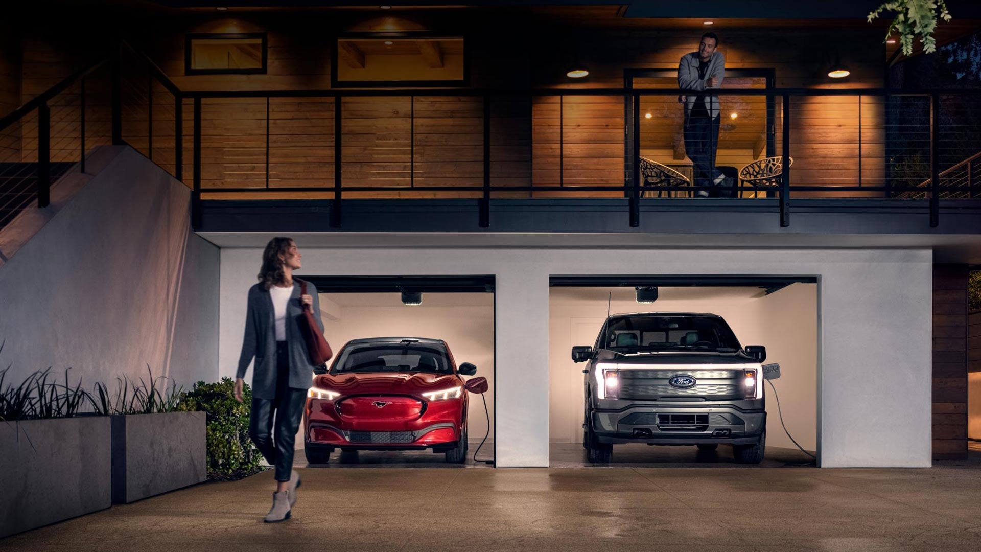 Woman walking out from home garage with a 2024 Mustang® Mach-E and Ford Lightning® truck in plugged-in and charging | Queen City Ford in Cincinnati OH